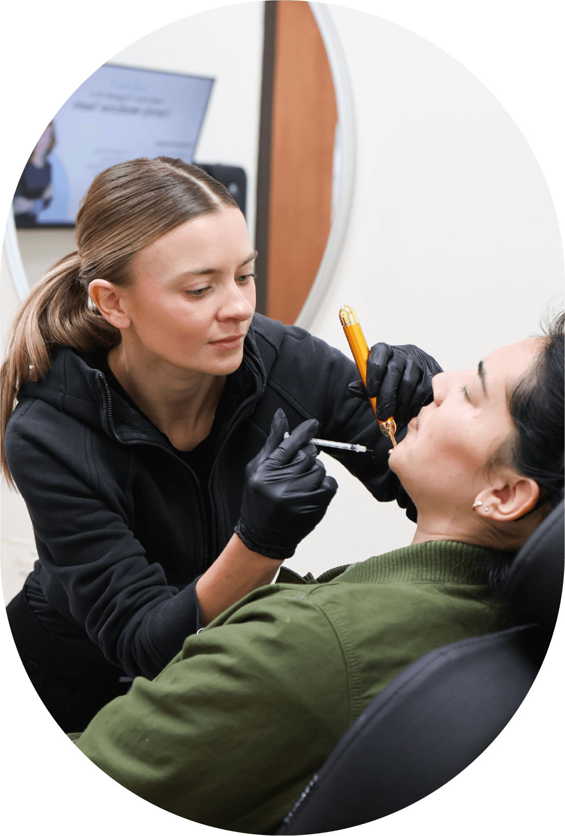 A technician wearing black gloves performs an injection on a client's face.
