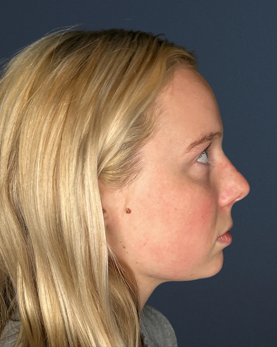 A profile photo of a young blonde woman against a dark blue background.