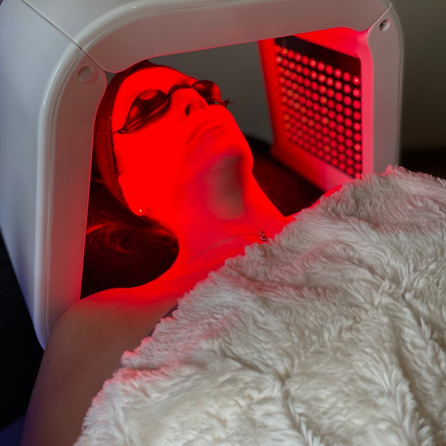 A woman receives red light therapy from an LED machine.