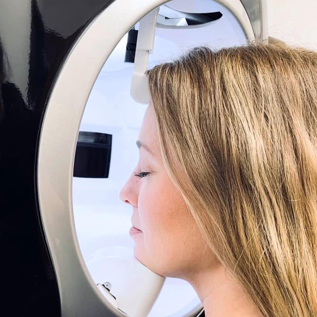 A woman rests her chin on the designated location while receiving a Skin Visia scan from a machine.
