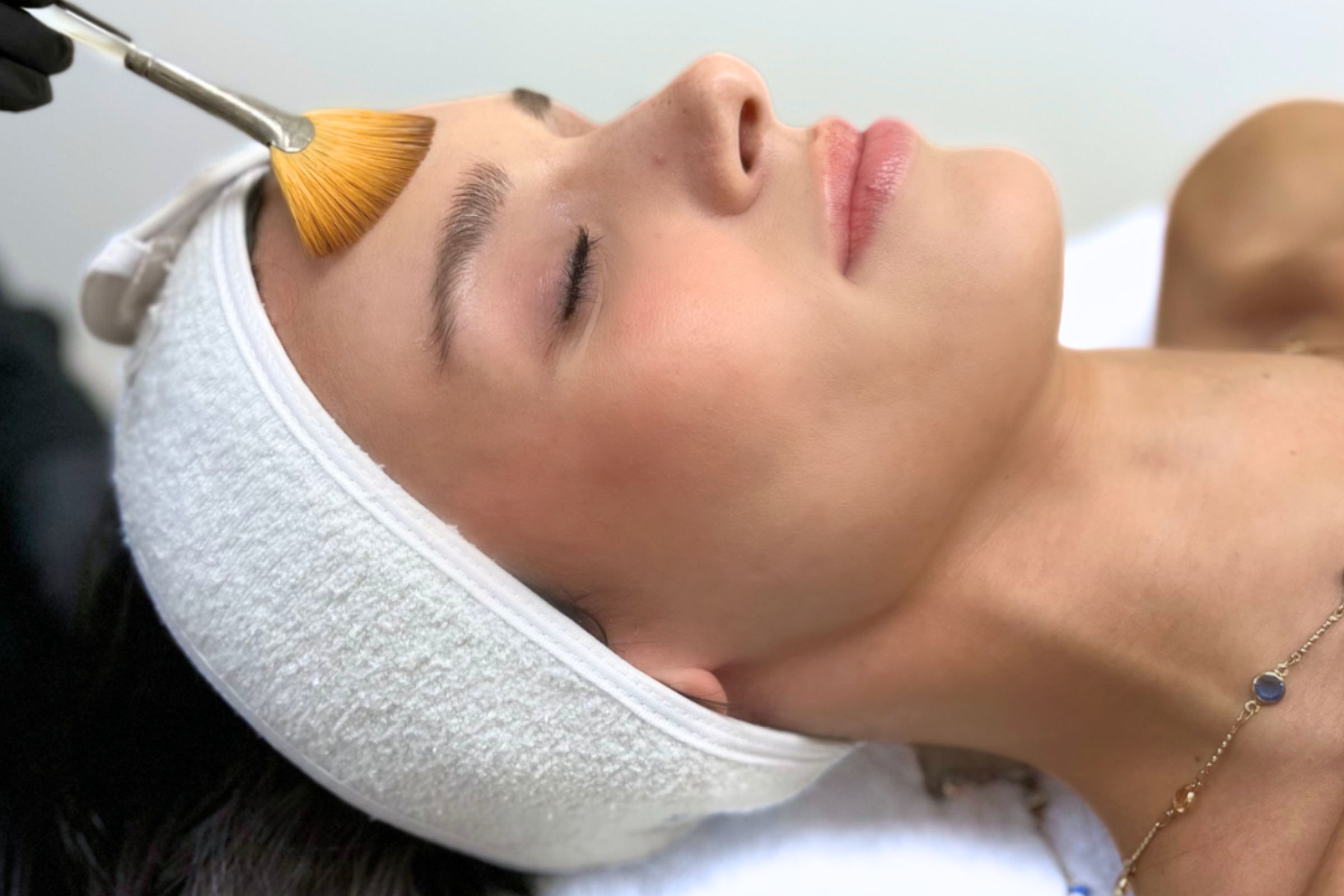 A white headband keeps a woman's hair back as she receives a deluxe oxyfacial.